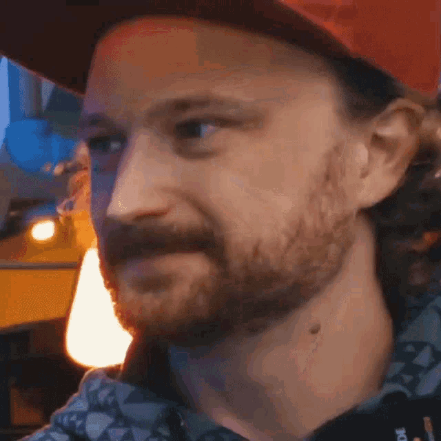 a man with a beard is wearing a red hat and a blue shirt