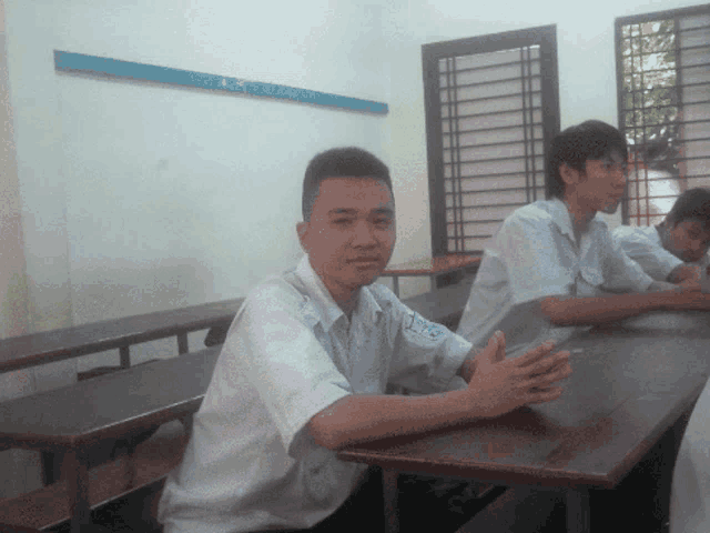 a young man sits at a desk with a sticker on his shirt that says ' a ' on it