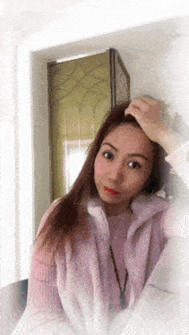 a woman in a pink sweater and a purple vest is touching her hair