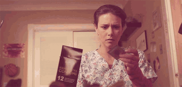a woman in a scrub top holds a box of men 's ultra condoms