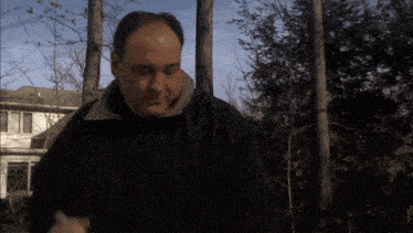 a man in a black jacket is standing in front of trees