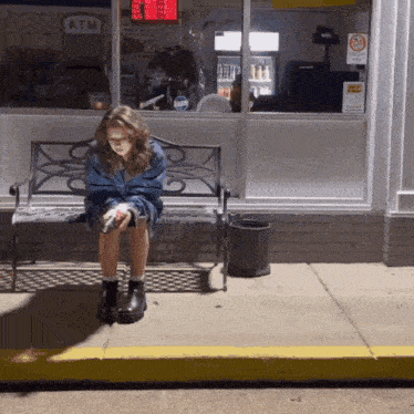 a girl sits on a bench in front of a store that says atm