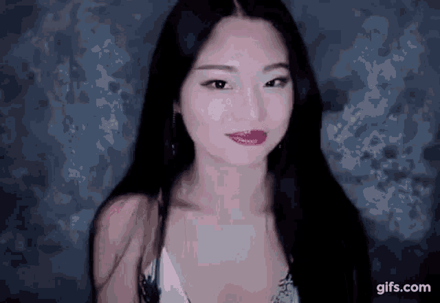 a woman with long black hair is standing in front of a black wall and looking at the camera .