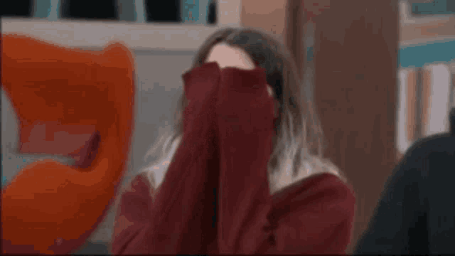 a woman in a red sweater is covering her face with her arms .