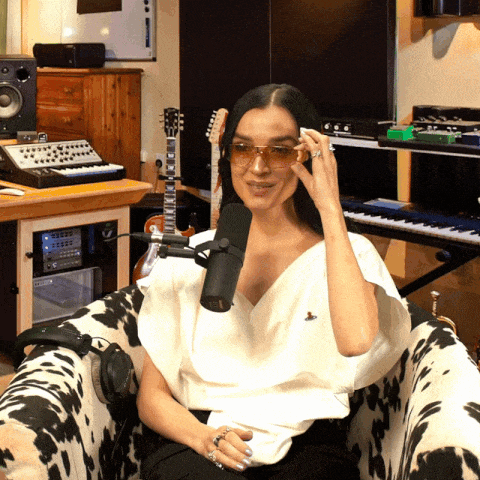a woman wearing sunglasses sits in front of a microphone in a studio