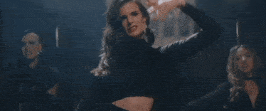 a woman in a black turtleneck is dancing in front of a building