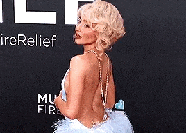 a woman is standing on a red carpet wearing a white dress with a feathered skirt .