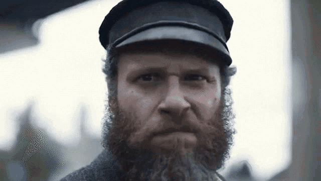 a man with a beard and hat is looking at the camera
