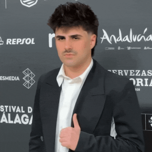 a man in a suit gives a thumbs up in front of a wall that says repsol on it
