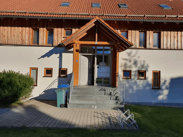 a white building with a wooden roof and a blue trash can in front of it