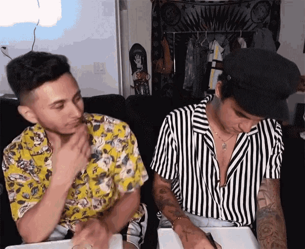 two men are sitting on a couch and one is wearing a yellow shirt