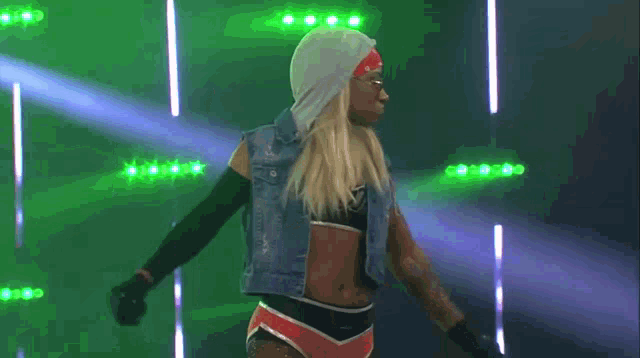 a woman in a denim vest is dancing in front of a row of lights