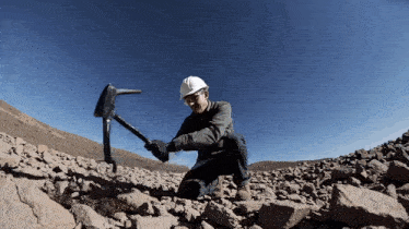 a man wearing a hard hat is kneeling down with a pickaxe in his hand