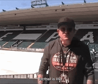a man wearing a shirt that says " football is life " stands in a stadium