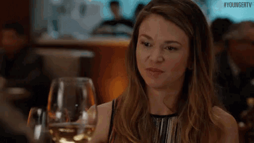 a woman is holding a glass of wine in her hand and making a funny face .