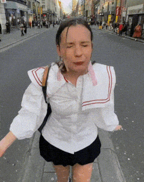 a woman wearing a white shirt and black skirt is walking down a street