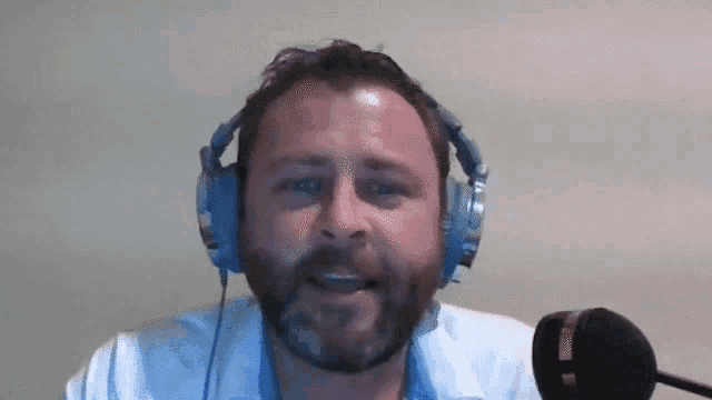 a man with a beard is wearing headphones and speaking into a microphone .