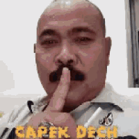 a man with a mustache is holding his finger to his mouth and says carek deh .