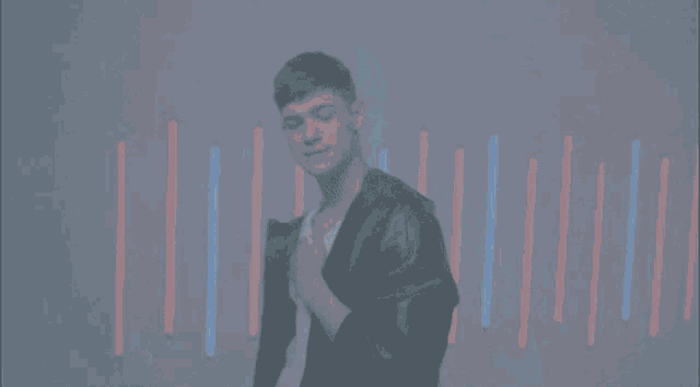 a man in a black jacket stands in front of a blue background with red and blue stripes