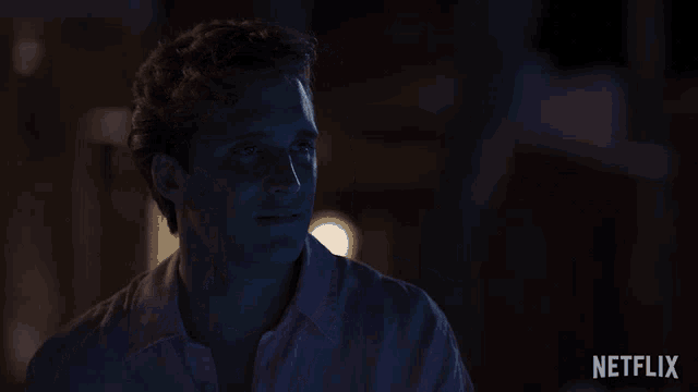 a man in a pink shirt is sitting in a dark room with a netflix logo behind him