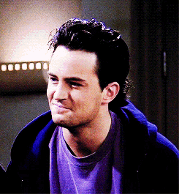 a close up of a man wearing a purple shirt and a blue hoodie