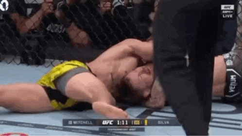 two men are wrestling in a boxing ring while a referee looks on .