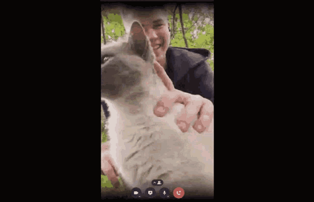 a young man is holding a cat in his arms and the cat is looking at the camera .