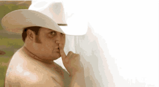 a shirtless man in a cowboy hat is holding his finger to his lips .