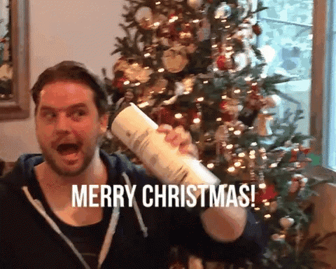 a man in front of a christmas tree is holding a piece of paper and says merry christmas