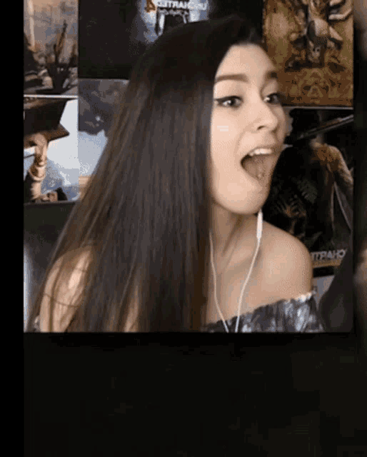 a woman wearing ear buds sticks her tongue out in front of a poster that says " strange "