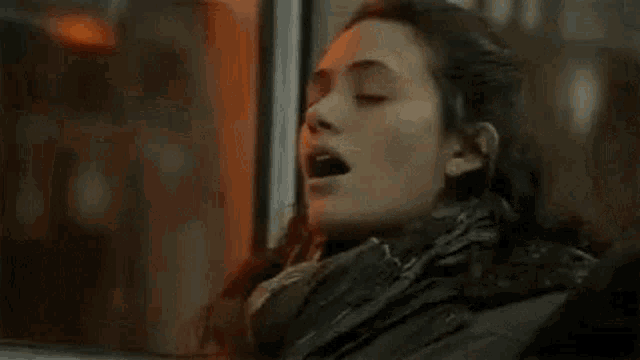 a woman is sitting in front of a window with her mouth open and her eyes closed .