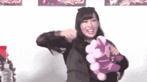a woman is holding a stuffed animal in her hands and smiling while standing in front of a wall .