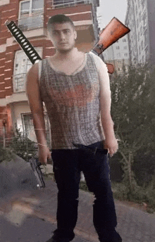 a man in a tank top is holding a gun and a sword in front of a building .