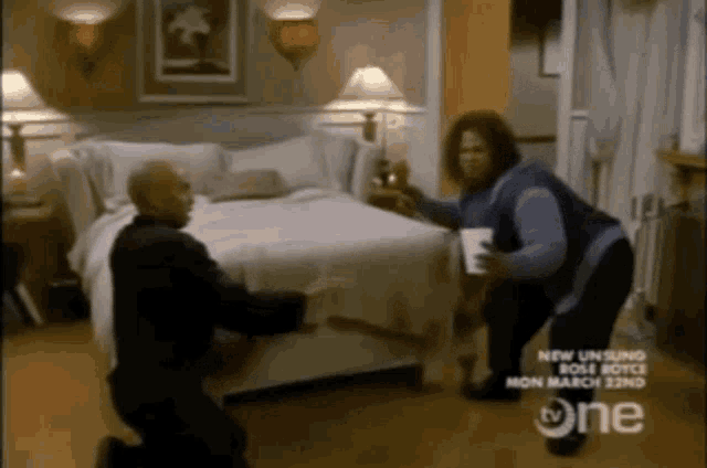 a man and a woman kneeling in front of a bed with a tv one ad in the corner