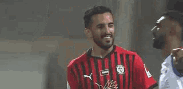 a soccer player in a red shirt is standing next to another soccer player in a white shirt .
