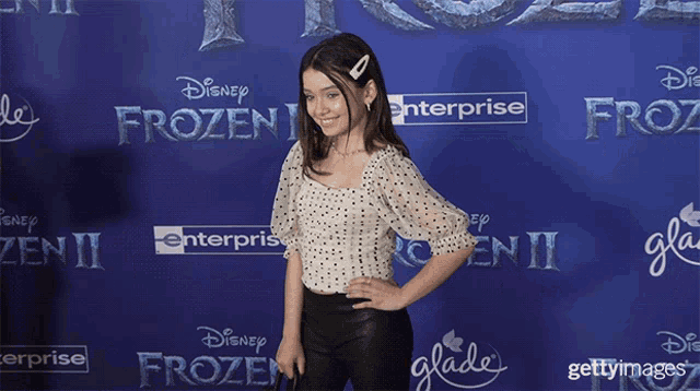 a girl stands in front of a blue carpet that says disney frozen ii