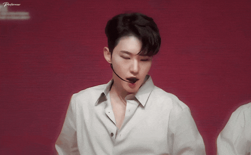 a man in a white shirt with a microphone in his mouth stands in front of a red background that says performer