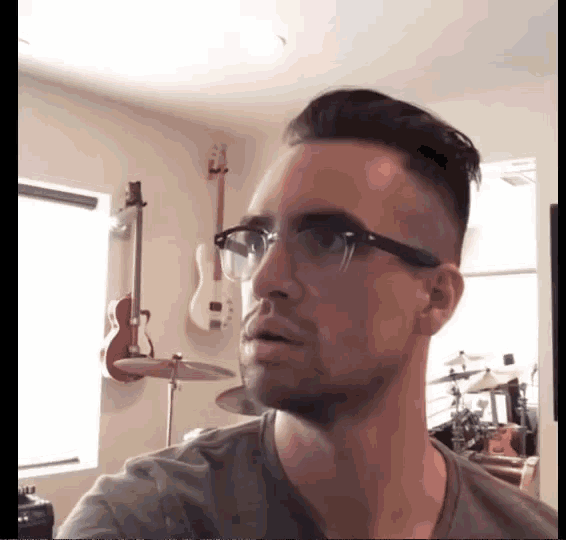 a man wearing glasses is standing in front of a drum set