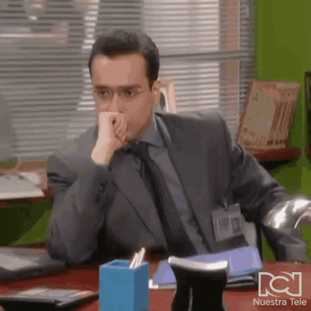 a man in a suit and tie is sitting at a desk with a nuestra tele logo on the bottom
