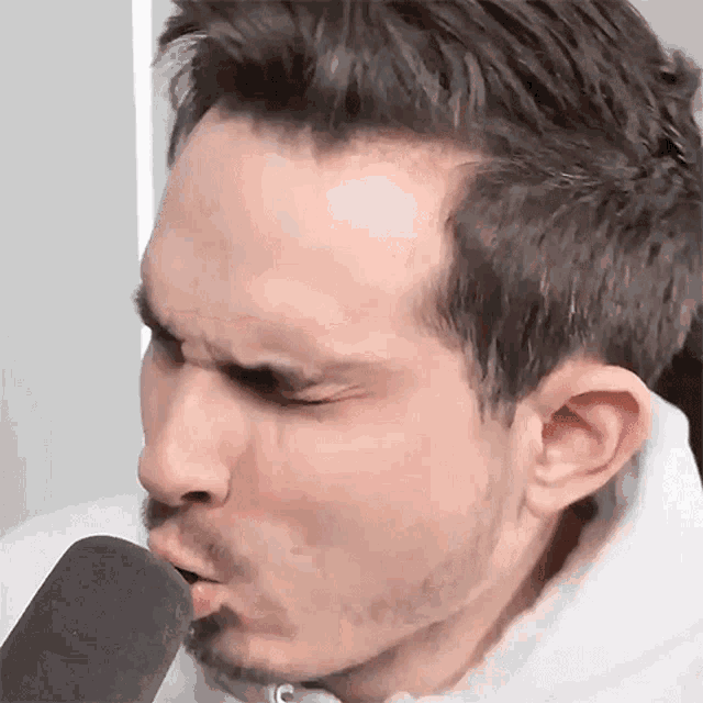 a man with a beard is blowing into a microphone with his eyes closed .