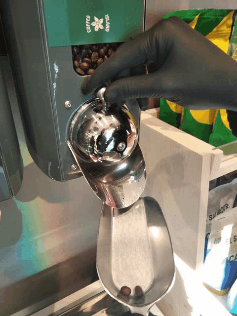 a person in black gloves is pouring coffee beans into a silver scoop