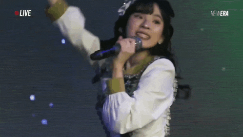 a woman is singing into a microphone on a stage in front of a live audience .