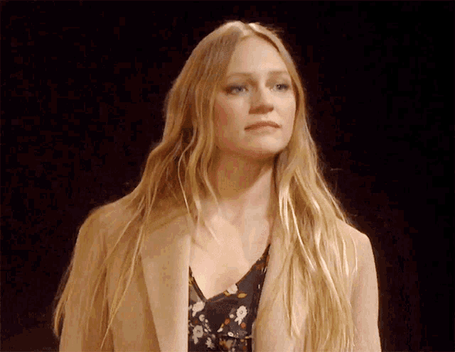 a woman with long blonde hair wearing a tan coat