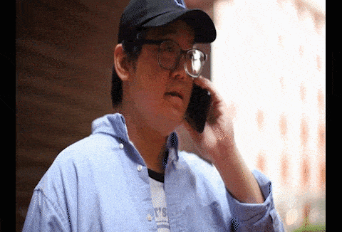 a man wearing glasses and a baseball cap is talking on a cell phone