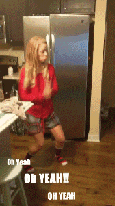 a woman in a red shirt and plaid shorts is dancing in front of a silver refrigerator