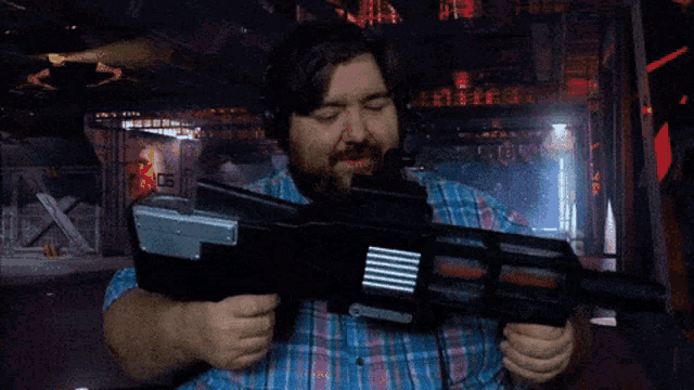 a man in a plaid shirt is holding a gun in front of a sign that says ' 02 ' on it