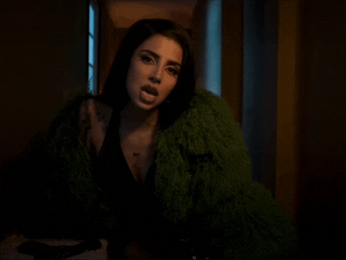 a woman in a green fur coat is sitting at a table holding a gun .