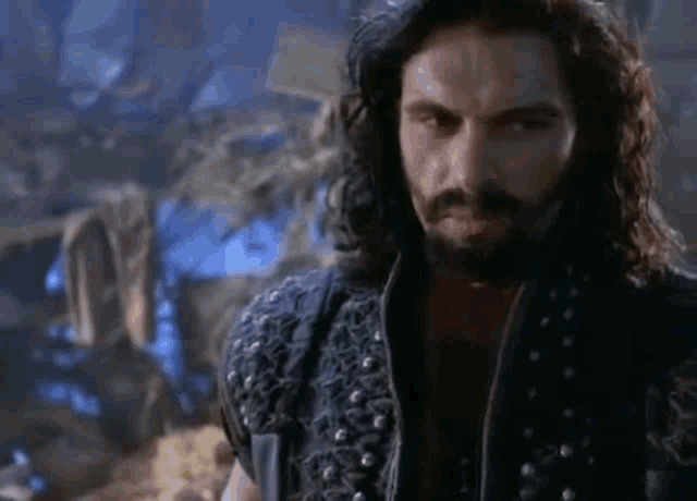a man with long hair and a beard is holding a knife in his hand .