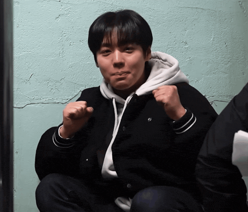 a man wearing a black jacket and a white hoodie has his fist up in the air