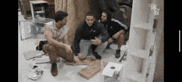 three men are squatting on the floor in front of a shelf that says coe moy
